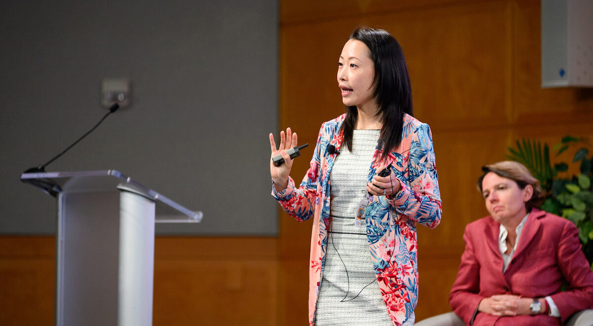A person presents at a conference, onstage near a podium
